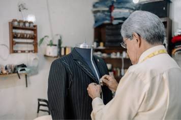 A photo of an older woman with silver hair taking a hearing assessment in a soundproof booth while an audiologist monitors the results.